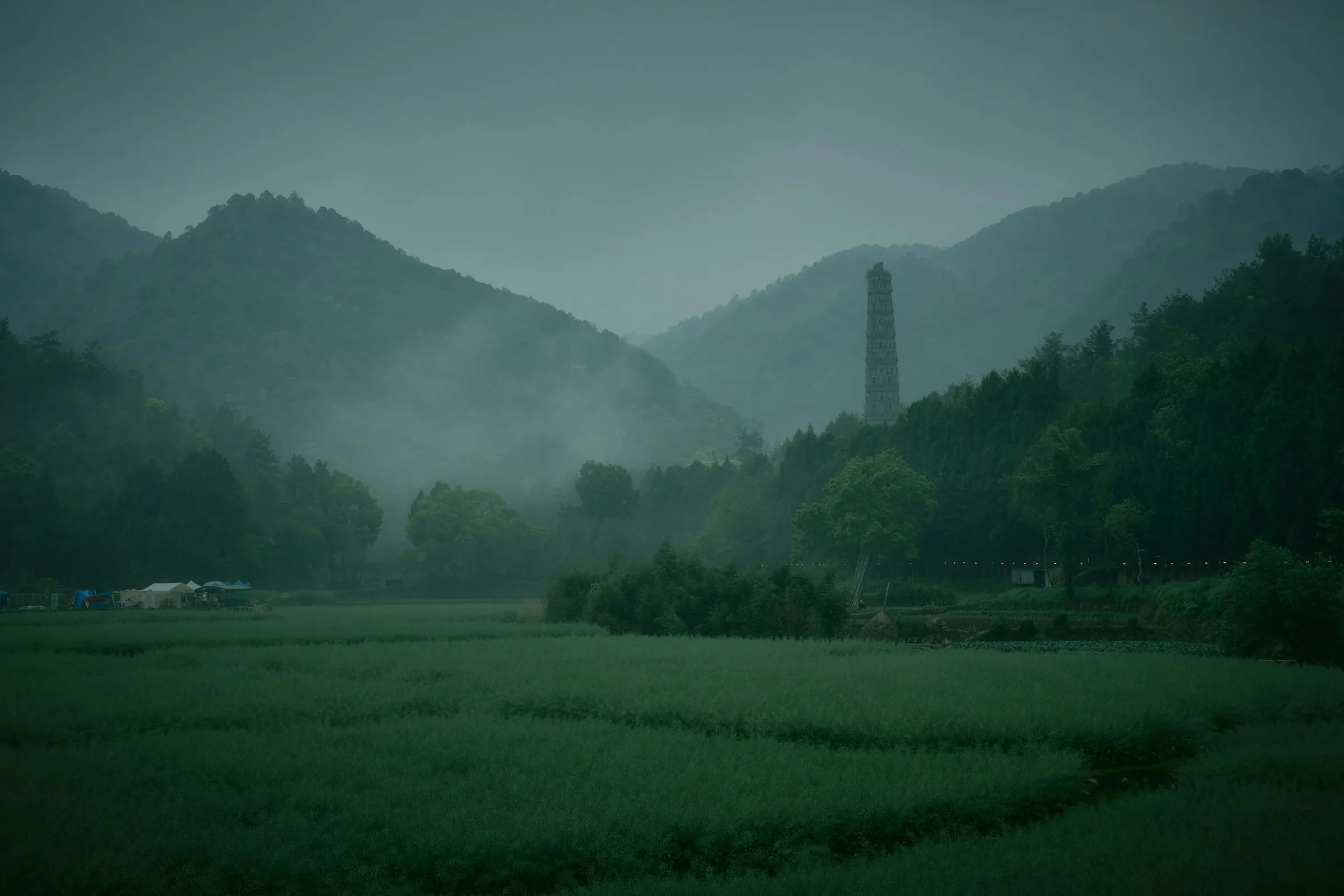 A Chinese watchtower (diaolou) rising above rice fields and mist in southern China.
